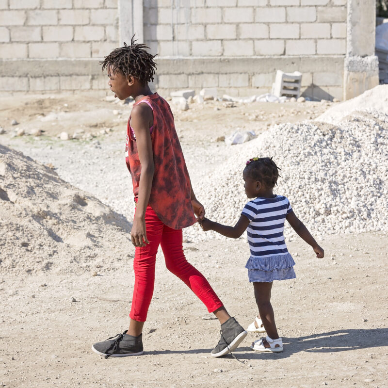 two haitian girls walk in a dirt lot